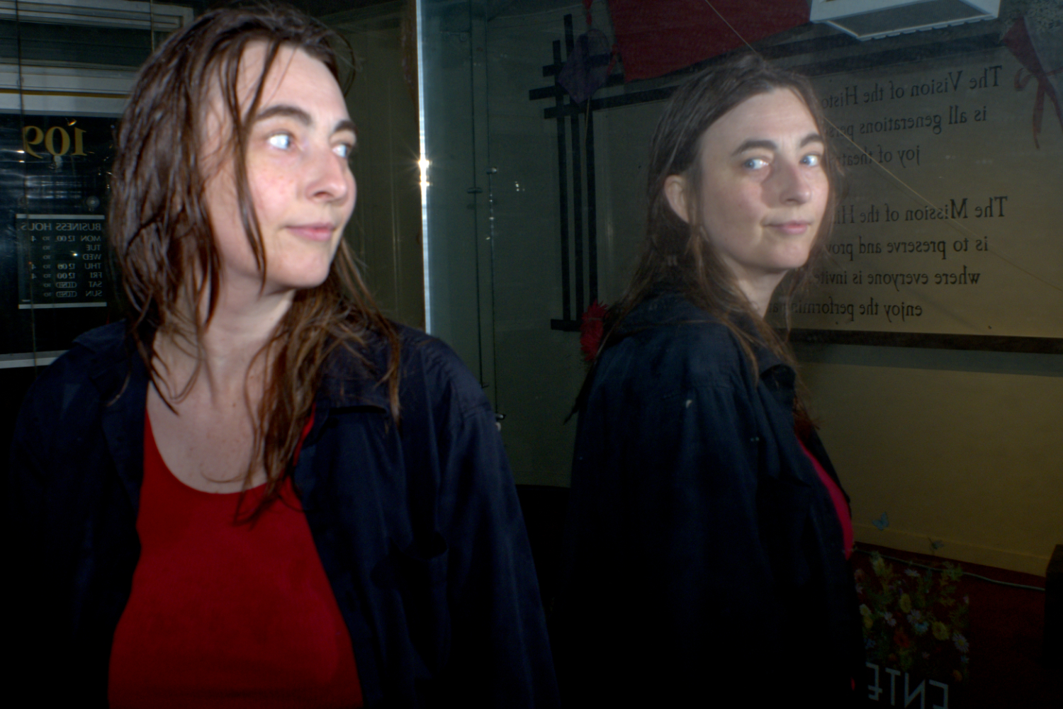 A white woman with auburn hair looking at her reflection in the rain at night